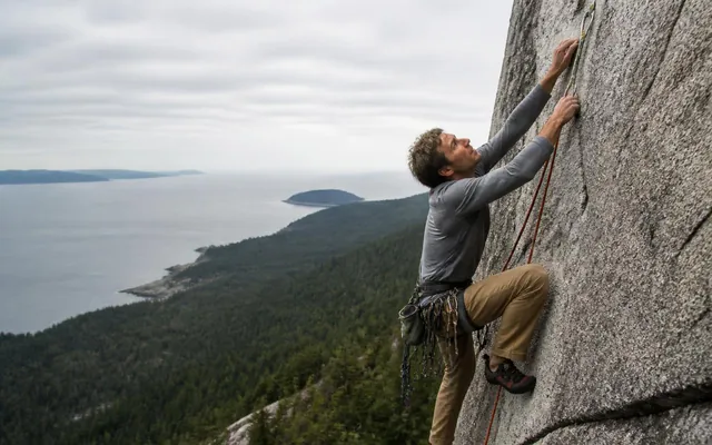 Climber on a granite wall above an ocean inlet